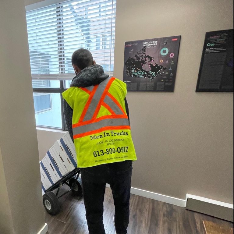 Men In Trucks mover in a branded high-visibility vest wheeling packed boxes on a dolly during an Ottawa move