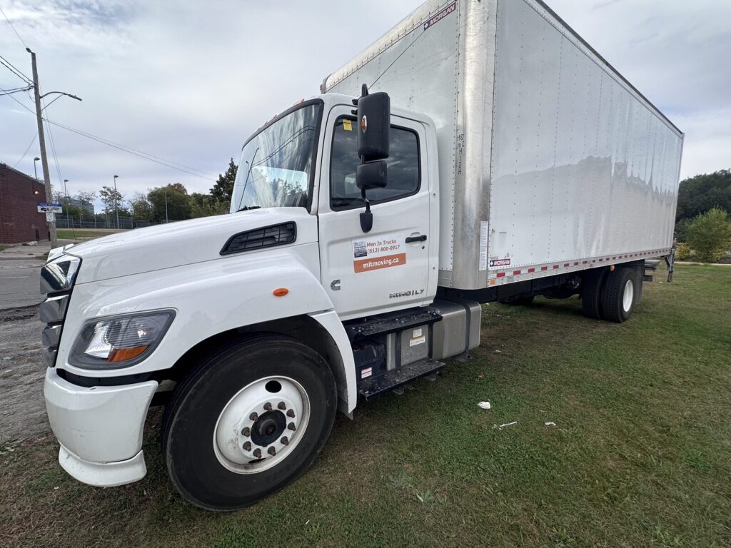 White box moving truck with a Men In Trucks decal on the cab door, parked on grass