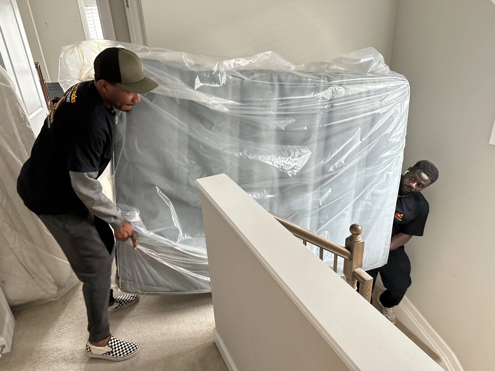 Men In Trucks movers carrying a wrapped mattress down the stairs of an Ottawa home