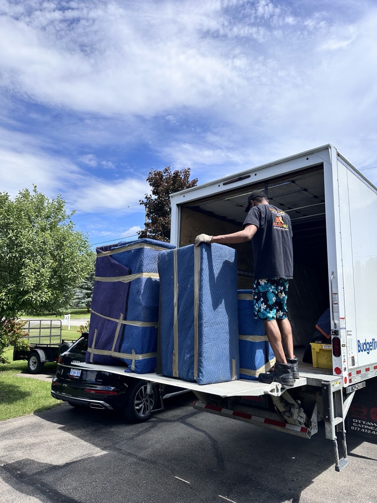 Men In Trucks mover loading wrapped mattresses on the truck liftgate outside an Ottawa home