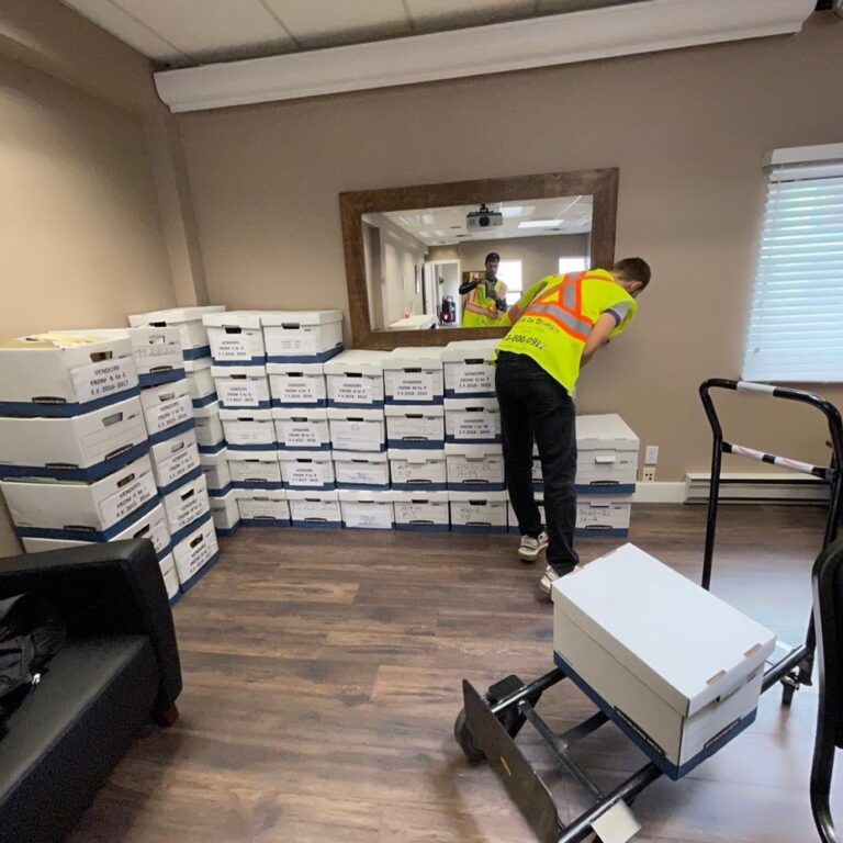 Mover in a hi-vis vest staging labelled file boxes beside a hand truck in an office.